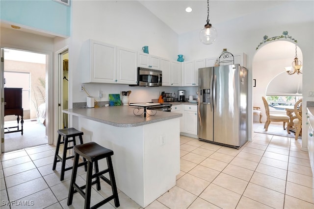 kitchen with high vaulted ceiling, stainless steel appliances, hanging light fixtures, light tile patterned floors, and white cabinets