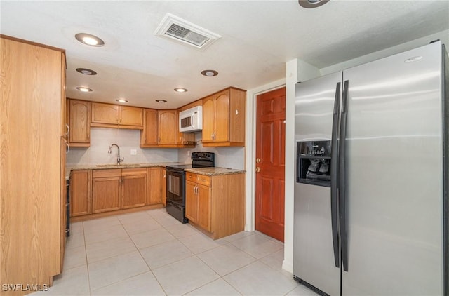 kitchen with light tile patterned floors, sink, black range with electric stovetop, stainless steel refrigerator with ice dispenser, and light stone counters