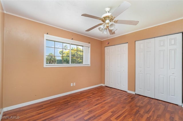 unfurnished bedroom featuring ornamental molding, dark hardwood / wood-style floors, two closets, and ceiling fan