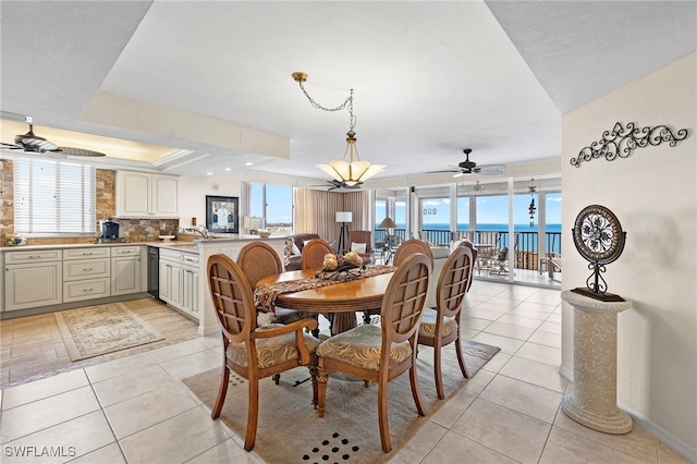 dining room with light tile patterned floors, sink, ceiling fan, a water view, and a raised ceiling