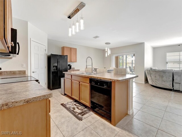 kitchen featuring black appliances, hanging light fixtures, sink, a center island with sink, and light tile patterned flooring