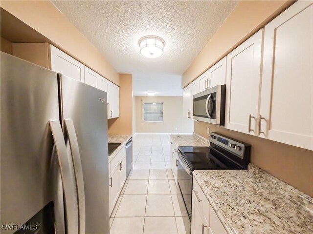 kitchen with a textured ceiling, light stone counters, appliances with stainless steel finishes, white cabinets, and light tile patterned flooring