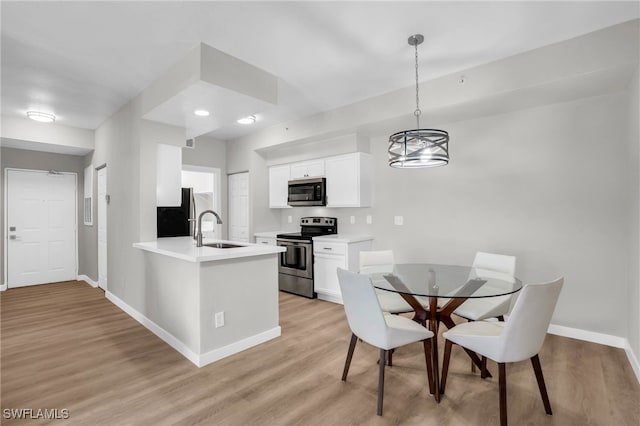 kitchen with appliances with stainless steel finishes, white cabinets, pendant lighting, light wood-type flooring, and sink