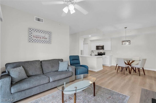 living room with baseboards, light wood finished floors, visible vents, and a ceiling fan