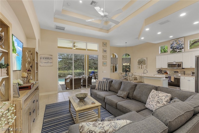 tiled living room with ceiling fan and a raised ceiling