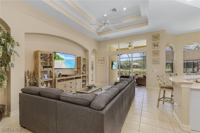 tiled living room with ceiling fan and a raised ceiling