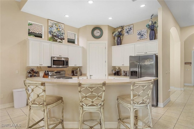 kitchen with light tile patterned floors, decorative backsplash, appliances with stainless steel finishes, a breakfast bar area, and white cabinetry