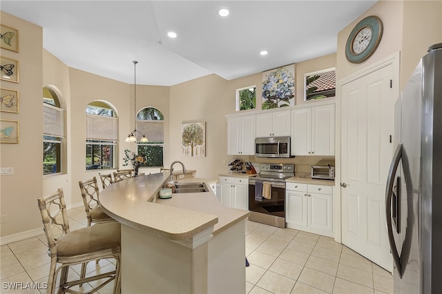 kitchen with stainless steel appliances, light tile patterned floors, sink, a kitchen bar, and decorative light fixtures