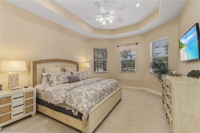 bedroom with light carpet, ceiling fan, and a raised ceiling