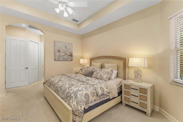 carpeted bedroom with ceiling fan, multiple windows, a raised ceiling, and a closet