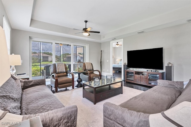 living room featuring a tray ceiling, ceiling fan, and light tile patterned floors