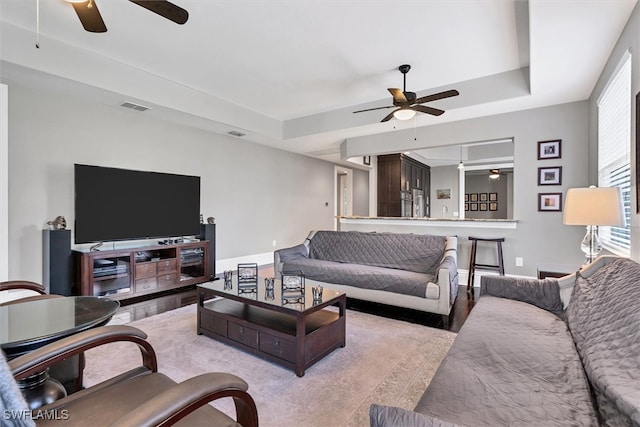 living room featuring ceiling fan, a raised ceiling, and light hardwood / wood-style floors