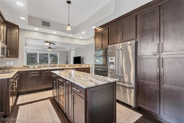 kitchen featuring ceiling fan, a raised ceiling, stainless steel appliances, and light stone counters