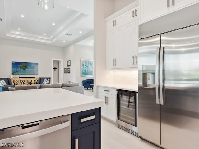 kitchen featuring a raised ceiling, tasteful backsplash, beverage cooler, white cabinets, and appliances with stainless steel finishes