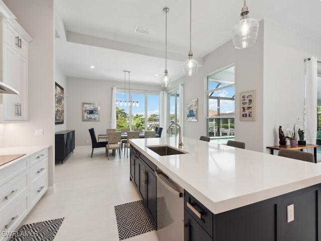 kitchen with sink, decorative light fixtures, dishwasher, white cabinetry, and a center island with sink