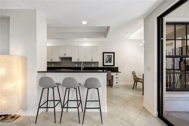 kitchen with decorative backsplash, a raised ceiling, white cabinets, light tile patterned flooring, and a breakfast bar