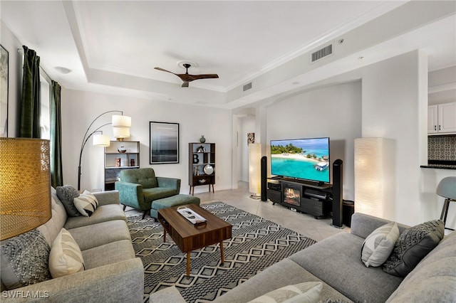 tiled living room with ceiling fan and a tray ceiling