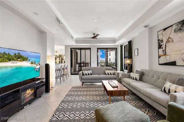 tiled living room with ceiling fan with notable chandelier, a raised ceiling, and ornamental molding