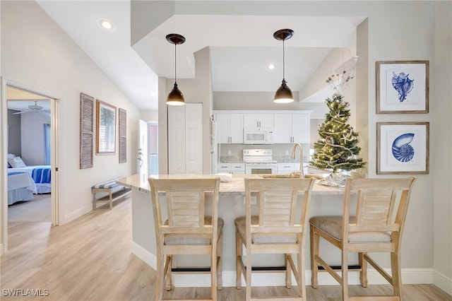 kitchen with a breakfast bar, white appliances, vaulted ceiling, pendant lighting, and white cabinetry