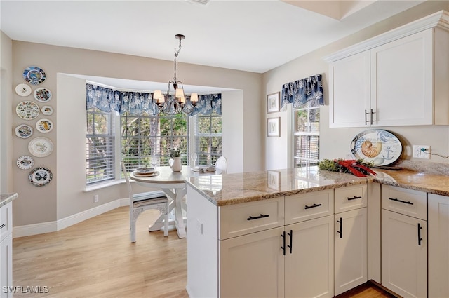 kitchen with light stone counters, kitchen peninsula, a chandelier, light hardwood / wood-style floors, and white cabinets