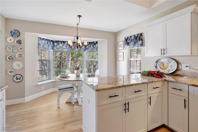 737 Wiggins Lake Dr Unit 201, Naples, FL 34110 - kitchen with a peninsula, a chandelier, light wood finished floors, white cabinets, and light stone countertops