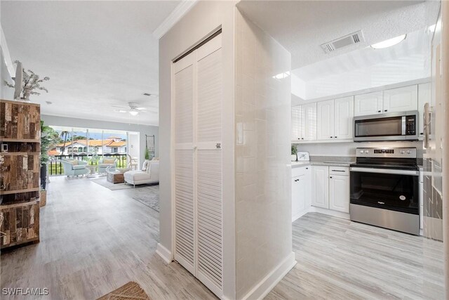 kitchen with white cabinets, crown molding, ceiling fan, appliances with stainless steel finishes, and light hardwood / wood-style floors