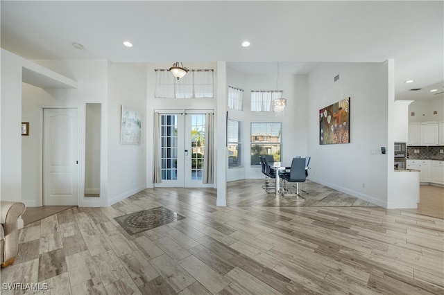 unfurnished living room with light hardwood / wood-style floors, a towering ceiling, and french doors