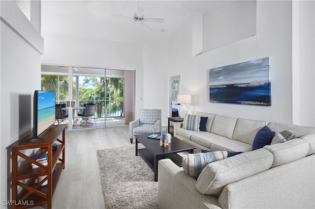 living room featuring a towering ceiling, light wood-type flooring, and ceiling fan