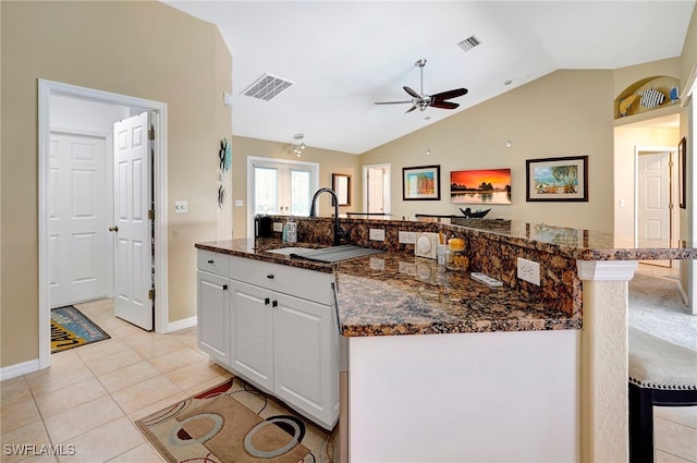 kitchen with ceiling fan, dark stone counters, vaulted ceiling, white cabinetry, and light tile patterned floors