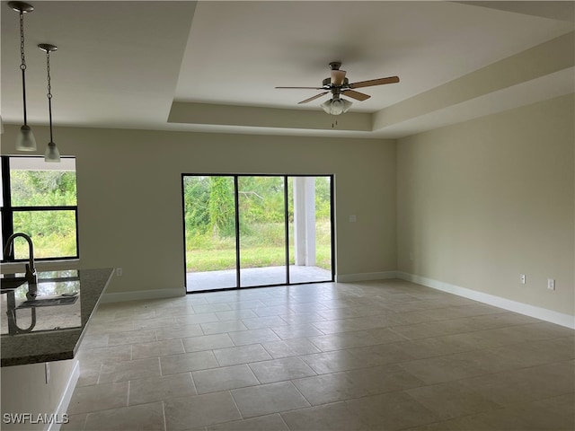 spare room featuring ceiling fan, a raised ceiling, light tile patterned floors, and a healthy amount of sunlight