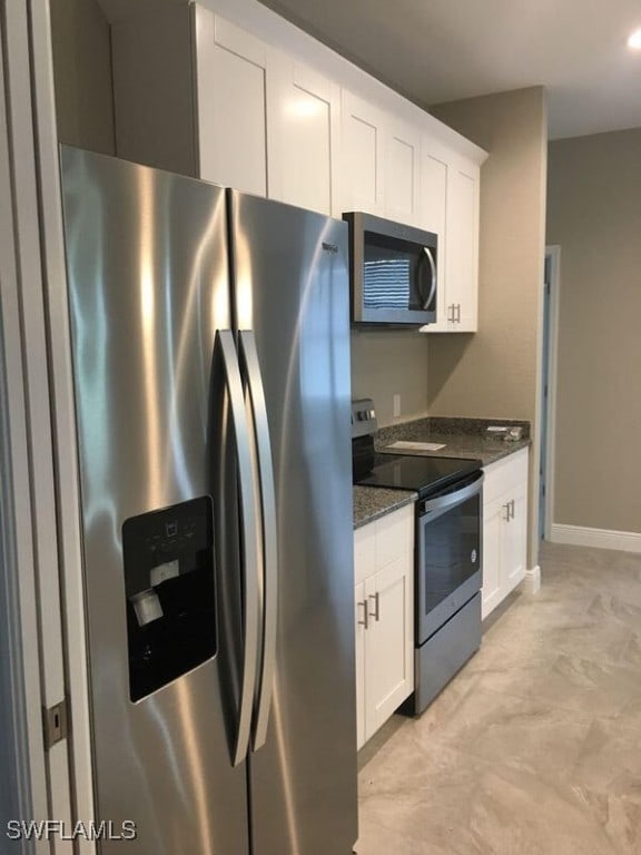 kitchen featuring light tile patterned floors, appliances with stainless steel finishes, dark stone countertops, and white cabinetry