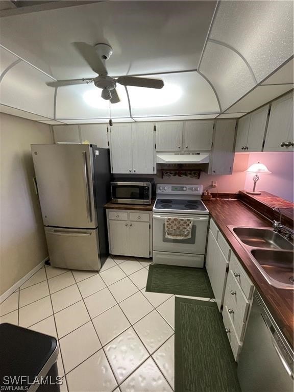 kitchen with appliances with stainless steel finishes, light tile patterned flooring, sink, and ceiling fan