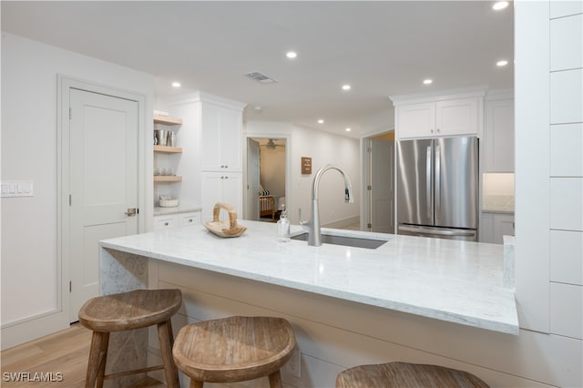 kitchen featuring light hardwood / wood-style flooring, white cabinetry, stainless steel refrigerator, sink, and a kitchen bar