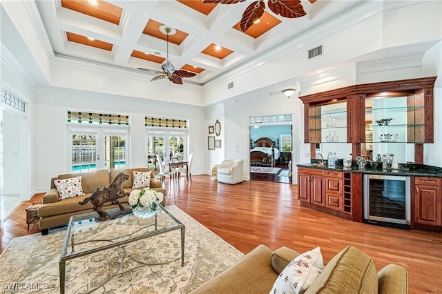 living room featuring beverage cooler, indoor bar, ceiling fan, beam ceiling, and coffered ceiling