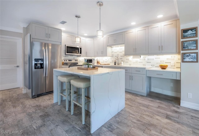 kitchen with sink, hanging light fixtures, appliances with stainless steel finishes, a kitchen island, and light hardwood / wood-style floors