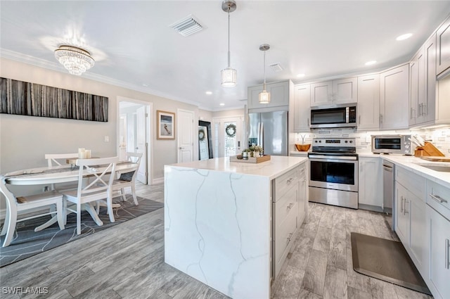 kitchen with appliances with stainless steel finishes, a center island, light hardwood / wood-style floors, decorative backsplash, and decorative light fixtures