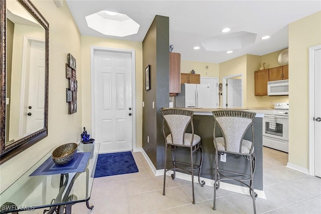 kitchen with light tile patterned floors, white appliances, a skylight, and a kitchen breakfast bar