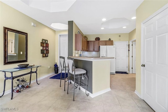 kitchen with light tile patterned floors, white refrigerator with ice dispenser, a kitchen breakfast bar, and kitchen peninsula