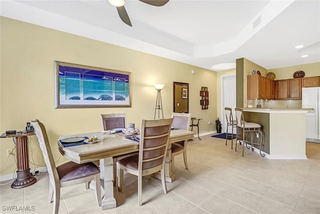 tiled dining room with ceiling fan and a tray ceiling