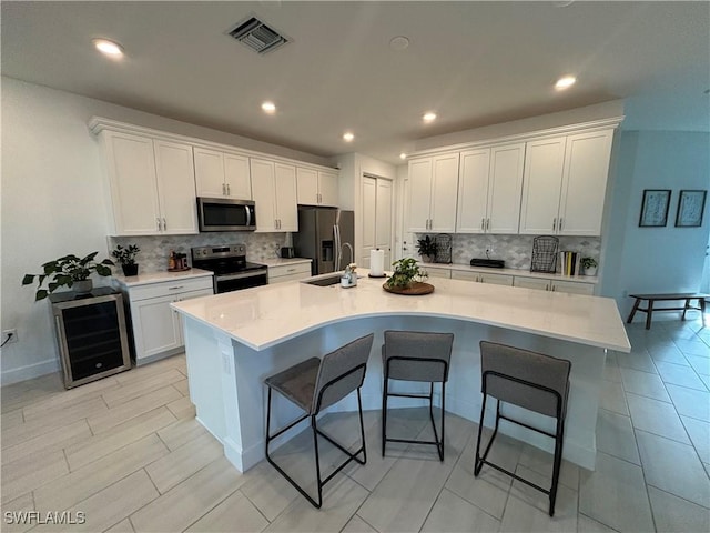 kitchen featuring white cabinets, stainless steel appliances, light countertops, and a large island with sink