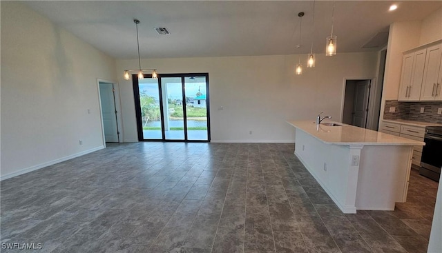 kitchen featuring hanging light fixtures, white cabinetry, a center island with sink, and backsplash