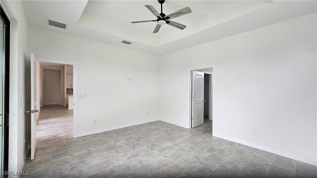 tiled spare room featuring ceiling fan and a raised ceiling