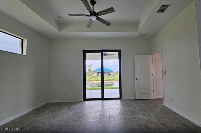 empty room with ceiling fan, tile patterned floors, and a tray ceiling