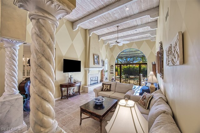 living room featuring wood ceiling, ceiling fan, a large fireplace, beamed ceiling, and ornate columns