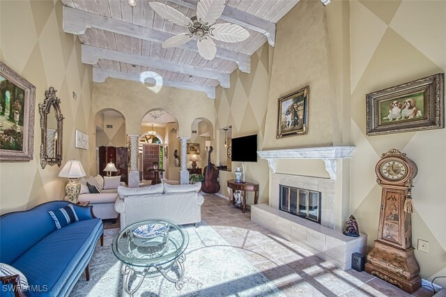 living room featuring ornate columns, wood ceiling, a tile fireplace, beamed ceiling, and ceiling fan