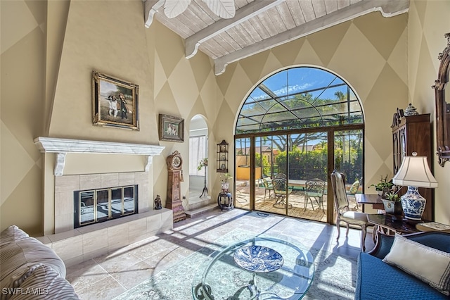 living room featuring beamed ceiling, wooden ceiling, a tile fireplace, and a high ceiling