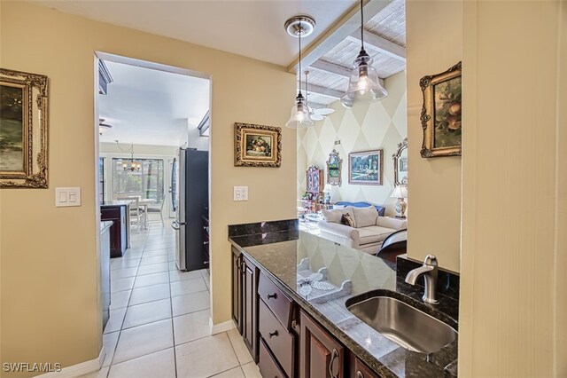 kitchen with sink, stainless steel fridge, dark stone countertops, dark brown cabinets, and decorative light fixtures