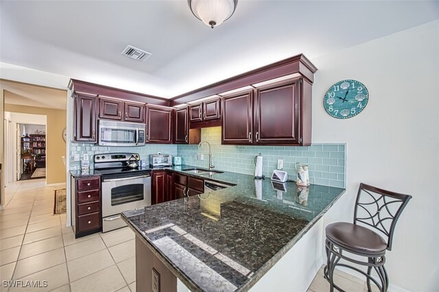 kitchen with appliances with stainless steel finishes, kitchen peninsula, sink, and dark stone counters