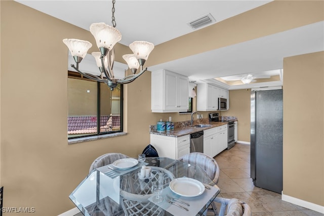 tiled dining space featuring ceiling fan with notable chandelier, sink, and a tray ceiling