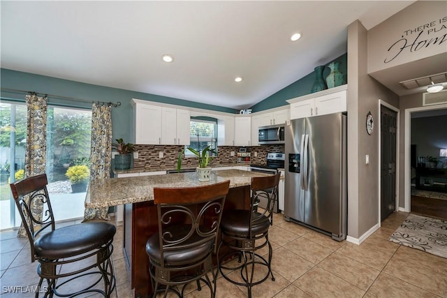 kitchen with light stone counters, white cabinetry, stainless steel appliances, and vaulted ceiling